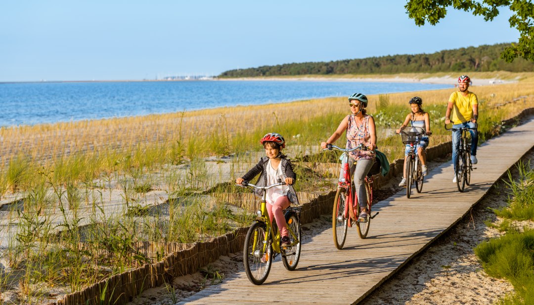 Eine vierköpfige Familie fährt mit dem Fahrrad auf dem Radweg am Strand entlang. // Von Kröslin über Freest bis zum Strand von Lubmin: Und Maja ist die Schnellste! // © MV-T/Tiemann Eine vierköpfige Familie fährt mit dem Fahrrad auf dem Radweg am Strand entlang.