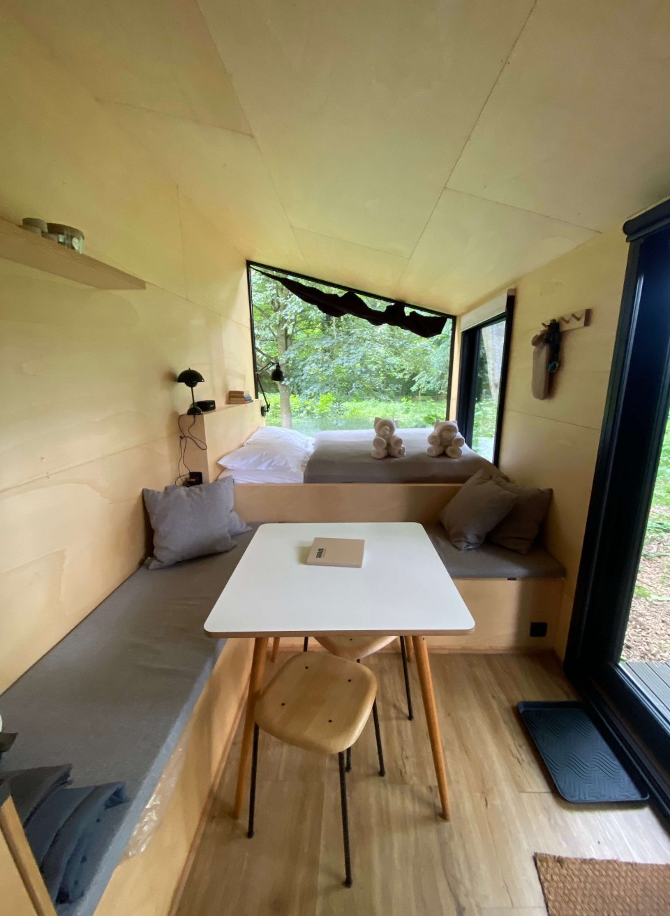 Heller Innenraum eines Tiny Houses bei Schloss Neuhoff mit gemütlicher Sitzecke, Bett und Waldblick. // Minimalistisch wohnen mitten in der Natur – der lichtdurchflutete Innenraum des Tiny Houses bei Schloss Neuhoff lädt zum Entspannen und Abschalten ein. // © Schloss Neuhoff Heller Innenraum eines Tiny Houses bei Schloss Neuhoff mit gemütlicher Sitzecke, Bett und Waldblick.