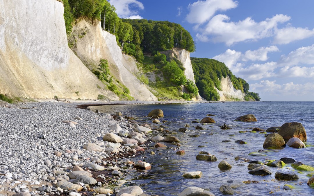 Leuchtend weiße Kreidefelsen ragen im Nationalpark Jasmund steil aus der Ostsee empor. Runde Steine säumen das klare Wasser, während dichter Buchenwald die Klippen krönt – ein Naturerbe auf Rügen, das die Kraft der Elemente spürbar macht. // © Francesco Carovillano Leuchtend weiße Kreidefelsen ragen im Nationalpark Jasmund steil aus der Ostsee empor. Runde Steine säumen das klare Wasser, während dichter Buchenwald die Klippen krönt – ein Naturerbe auf Rügen, das die Kraft der Elemente spürbar macht. // © Francesco Carovillano