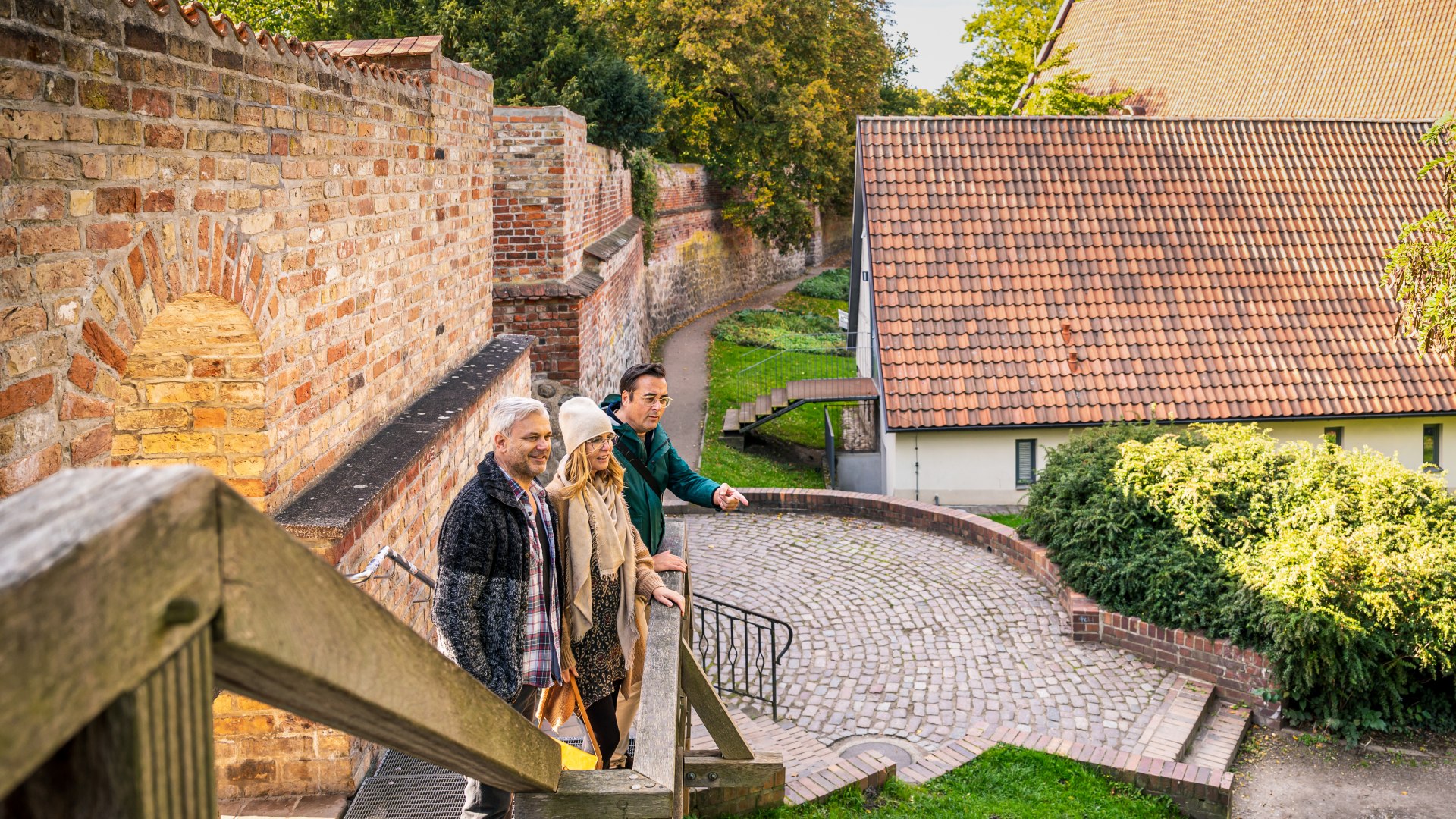 Drei Personen stehen an der alten Stadtmauer in Rostock und schauen auf den "Innenhof" // Bei den Rundgängen lernen Gäste auch Sehenswürdigkeiten Rostocks kennen – hier die alte Stadtmauer // © MV-T/Tiemann Drei Personen stehen an der alten Stadtmauer in Rostock und schauen auf den "Innenhof"