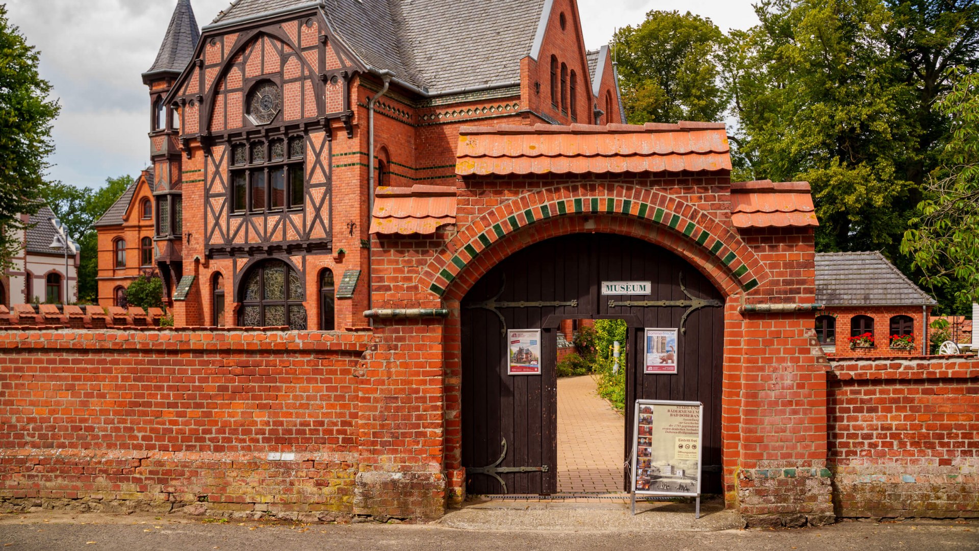 Das Stadt- und B&auml;dermuseum im M&ouml;ckelhaus in Bad Doberan, ein historisches Geb&auml;ude mit markanter Backstein- und Fachwerkarchitektur, umgeben von einer roten Backsteinmauer.