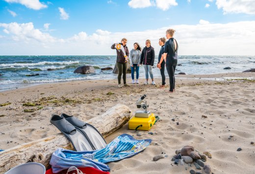 Mit den Urlaubsrangern am Strand von G&ouml;hren - Kinder stehen mit einer Rangerin am Strand und forschen.