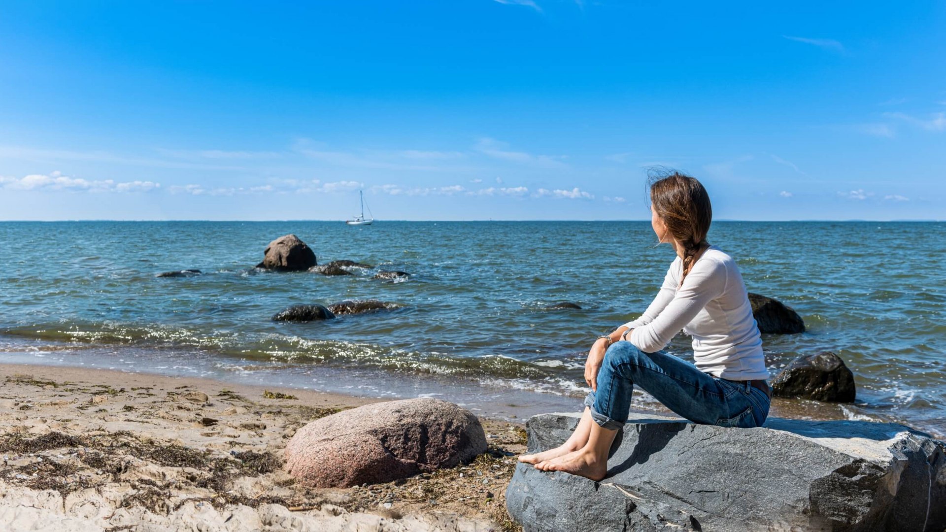Ein Vorbild für eine Skizze: Vom Strand aus schaut man auf die Ostsee. Am Strand liegen eine handvoll große Steine und am Horizont ein Segelboot.