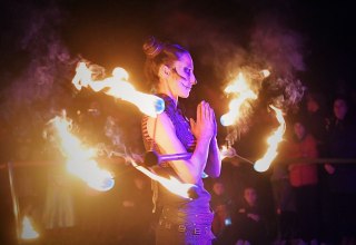 Beim Lampionfest im Zoo Rostock führt eine Frau mit Gesichtsschminke eine Feuershow vor und hält einen brennenden Stab in der Hand. // © Zoo Rostock/ Kloock Beim Lampionfest im Zoo Rostock führt eine Frau mit Gesichtsschminke eine Feuershow vor und hält einen brennenden Stab in der Hand. // © Zoo Rostock/ Kloock