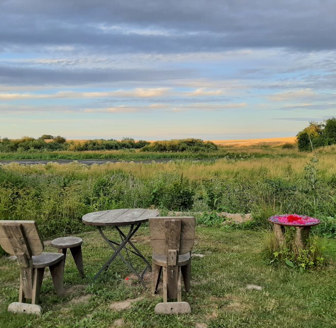 Der Sitzplatz am Weiher mit 2 Stühlen, 2 Hockern und 1 Tisch aus Holz. Der Blick geht über den Gartenrand und den zeitweise ausgetrockneten Weiher in die Landschaft. // © Mirabell e.V. Der Sitzplatz am Weiher mit 2 Stühlen, 2 Hockern und 1 Tisch aus Holz. Der Blick geht über den Gartenrand und den zeitweise ausgetrockneten Weiher in die Landschaft. // © Mirabell e.V.