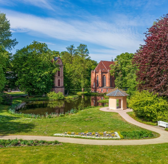 Glockenturm und Parkgeb&auml;ude im Schlossgarten Ludwigslust mit Blumen und B&auml;umen.