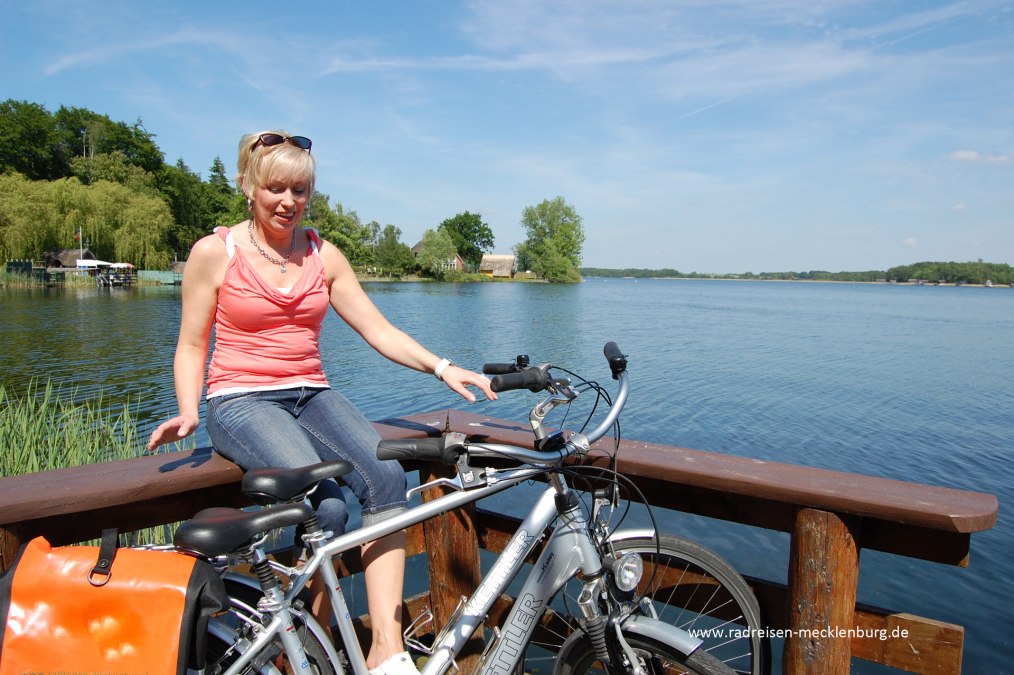 Eine Radfahrerin sitzt auf Geländer am See., © Ralf Tetmeyer, radreisen-mecklenburg Eine Radfahrerin sitzt auf Geländer am See., © Ralf Tetmeyer, radreisen-mecklenburg
