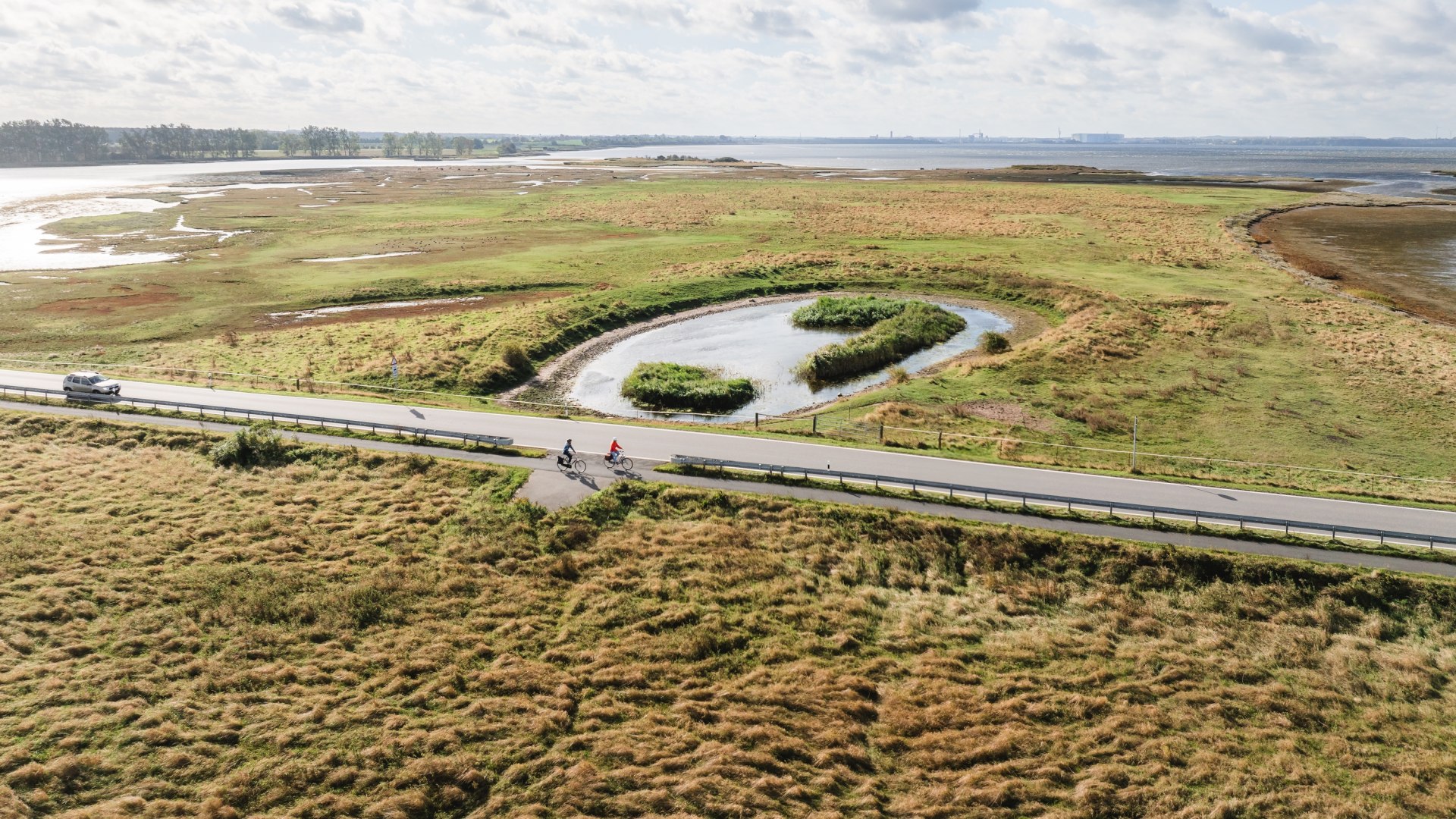 Luftaufnahme von Radfahrern auf einer Stra&szlig;e, die durch die gr&uuml;ne K&uuml;stenlandschaft der Insel Poel f&uuml;hrt.