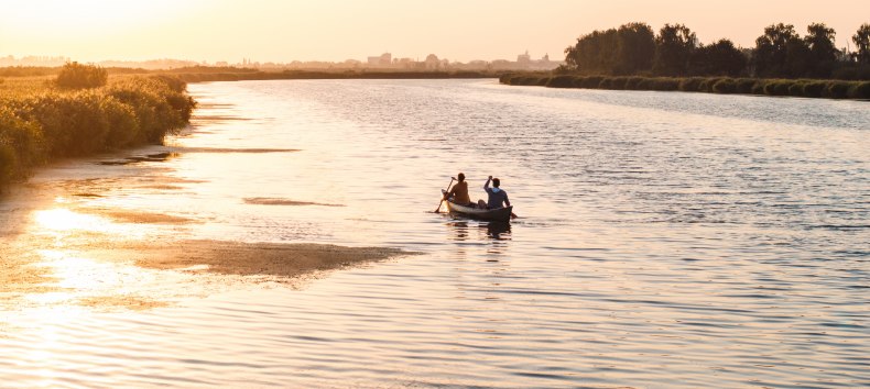 Zwei Personen paddeln in einem Kanu über einen ruhigen Fluss bei Sonnenuntergang, mit goldenem Licht auf dem Wasser. // Naturerlebnis auf dem Wasser – Eine idyllische Kanufahrt bei Sonnenuntergang entlang eines ruhigen Flusses, umgeben von sanften Uferlandschaften. // © MV-T/Gross Zwei Personen paddeln in einem Kanu über einen ruhigen Fluss bei Sonnenuntergang, mit goldenem Licht auf dem Wasser.