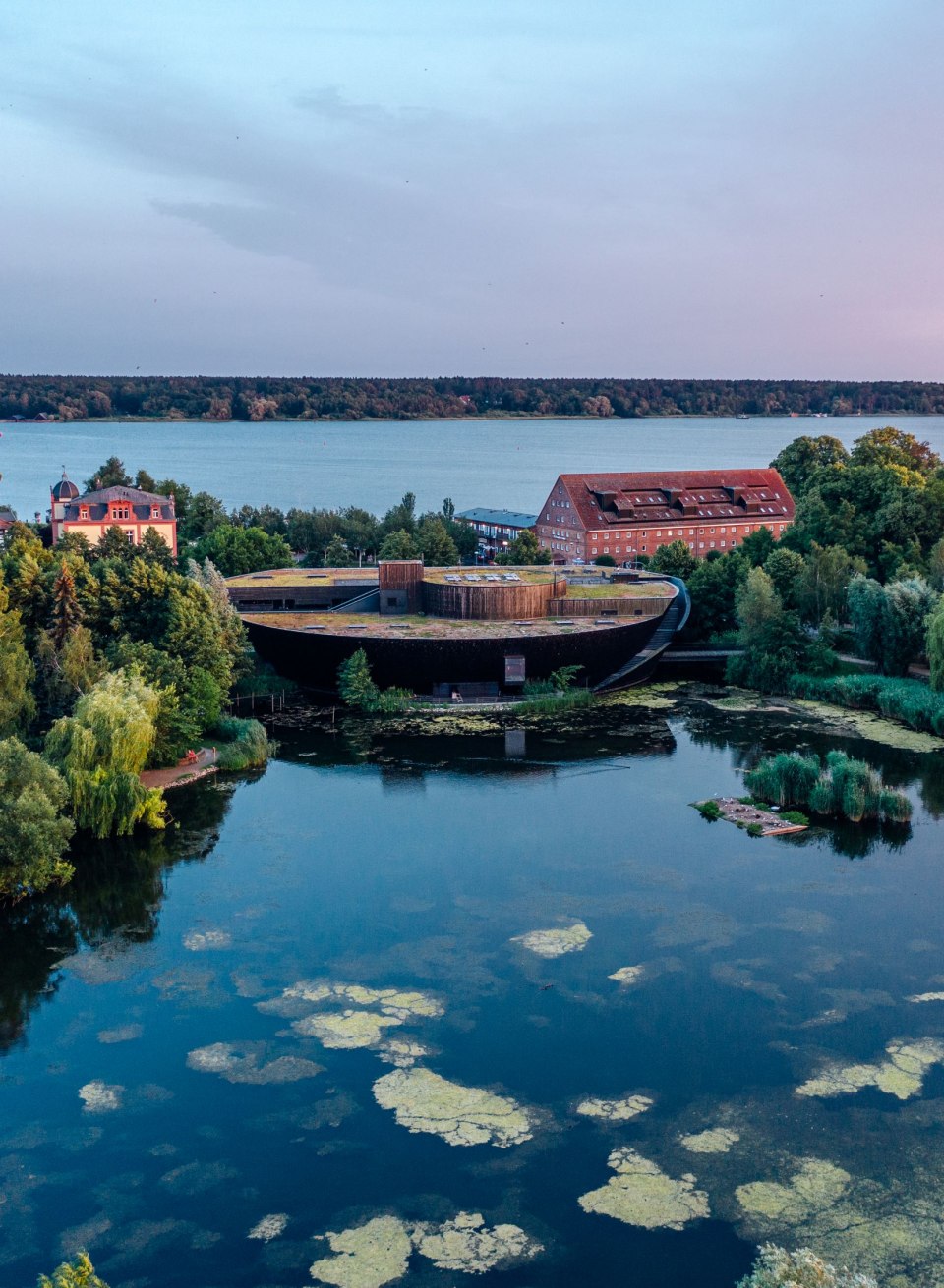 Luftaufnahme des M&uuml;ritzeums in Waren (M&uuml;ritz), umgeben von Wasser und gr&uuml;ner Natur in der Abendd&auml;mmerung.