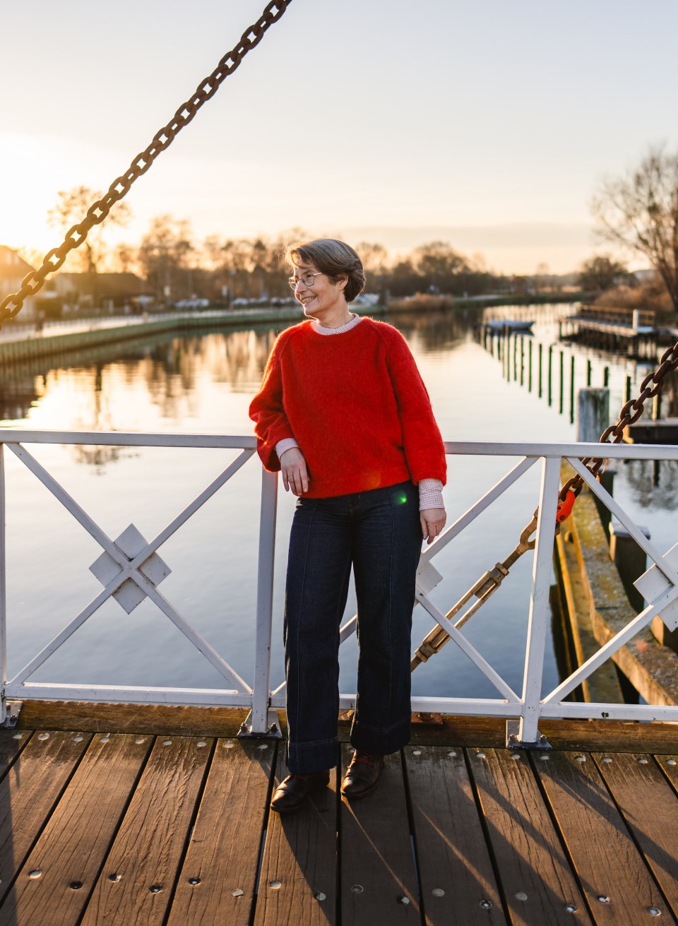 Frau auf der wei&szlig;en Wiecker Klappbr&uuml;cke bei Sonnenuntergang, im Hintergrund spiegelt sich der Ryck in Greifswald.