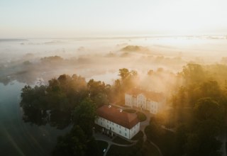 Goldenes Licht taucht Schloss Mirow in eine mystische Atmosph&auml;re. Nebelschwaden ziehen &uuml;ber die Seenlandschaft der Mecklenburgischen Seenplatte und lassen das historische Ensemble aus dem 18. Jahrhundert wie aus der Zeit gefallen wirken. Ein Moment purer Stille zwischen Wasser und Wald., &copy; 1000seen.de