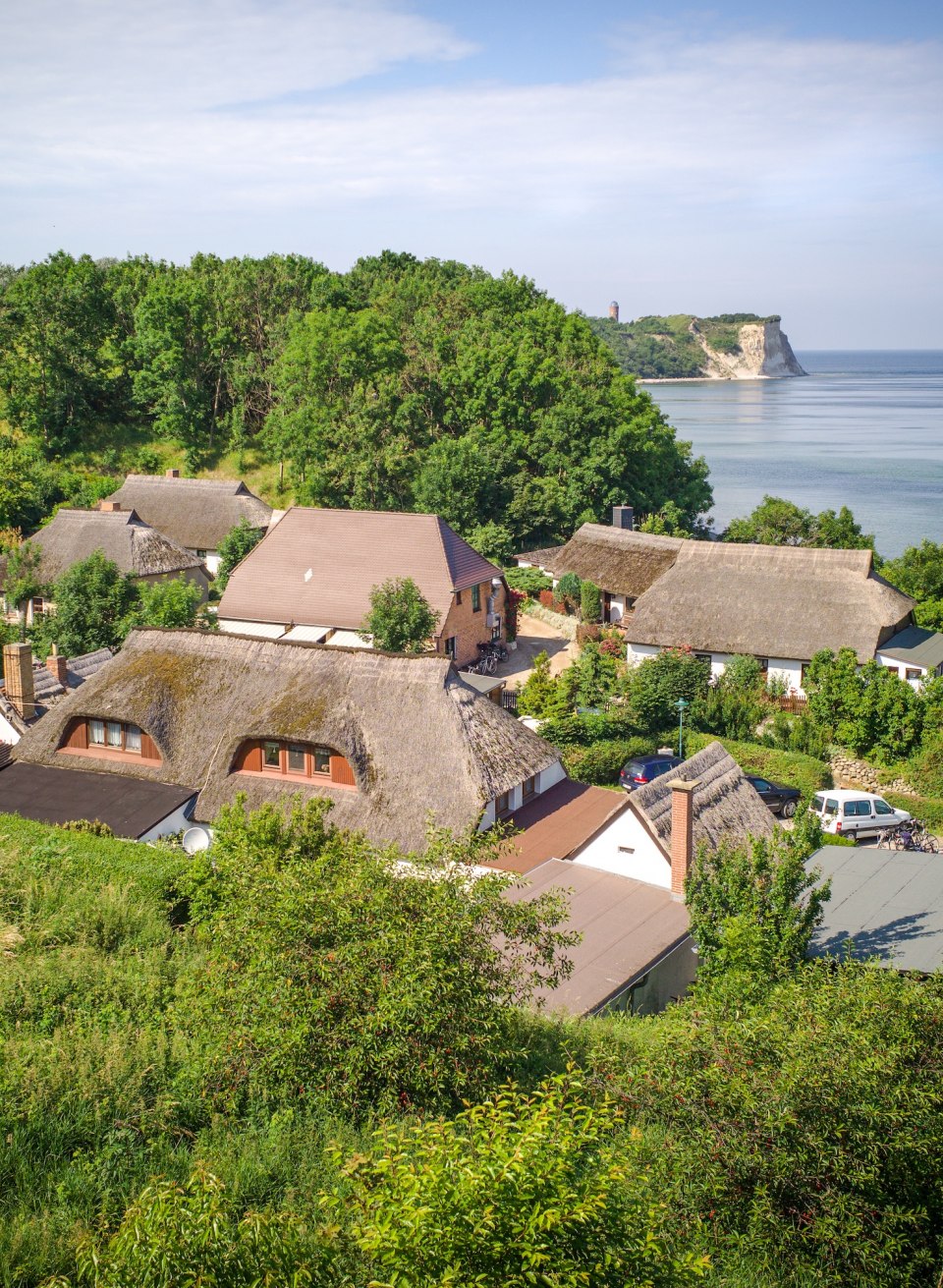 Fischerdorf Vitt auf der Insel R&uuml;gen mit traditionellen Reetdachh&auml;usern, umgeben von gr&uuml;ner Natur, im Hintergrund die Steilk&uuml;ste von Kap Arkona und die Ostsee.
