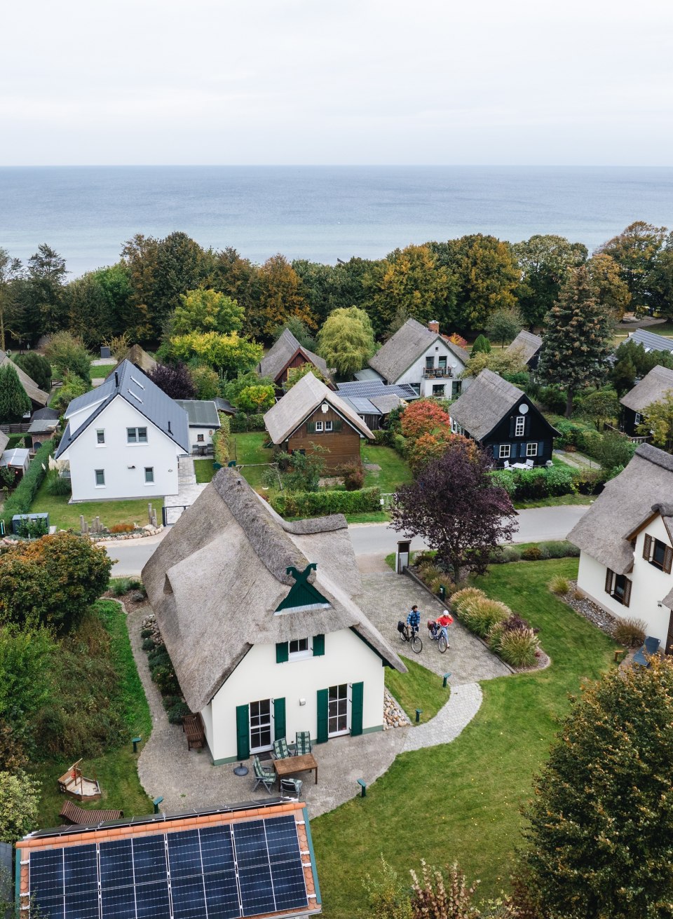  Luftaufnahme von Reetdachh&auml;usern auf der Insel Poel, umgeben von gr&uuml;nen G&auml;rten und mit Blick auf die Ostsee.