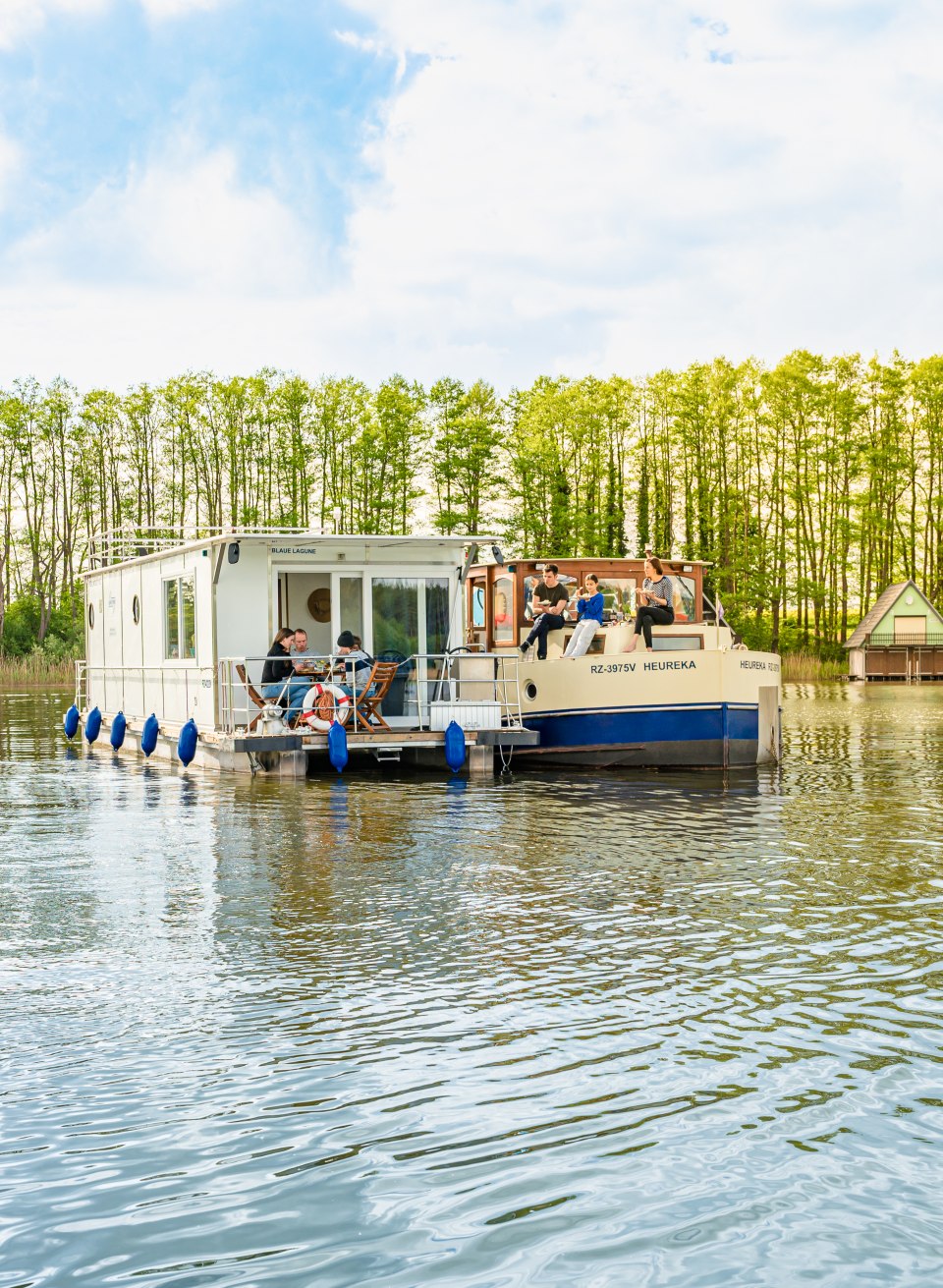 Zwei Hausboote liegen neben einander mit jeweils einer Familie und sie essen Kuchen. // Obwohl jede der beiden Familien ein eigenes Hausboot hat, verbringen sie fast jede Minute ihres Urlaubs miteinander. So auch die Kuchenpausen, für die sie ihre Boote nebeneinanderlegen. // © MV-T/Tiemann Zwei Hausboote liegen neben einander mit jeweils einer Familie und sie essen Kuchen.