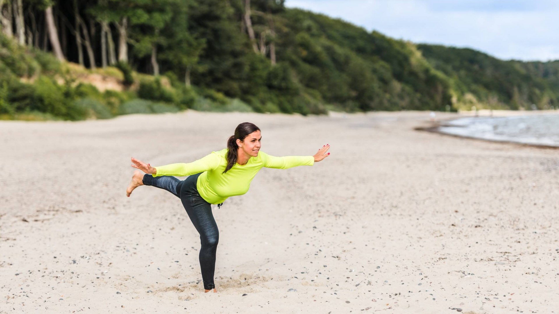 Eine Frau macht die "Standwaage" am Strand und h&auml;lt das Gleichgewicht.
