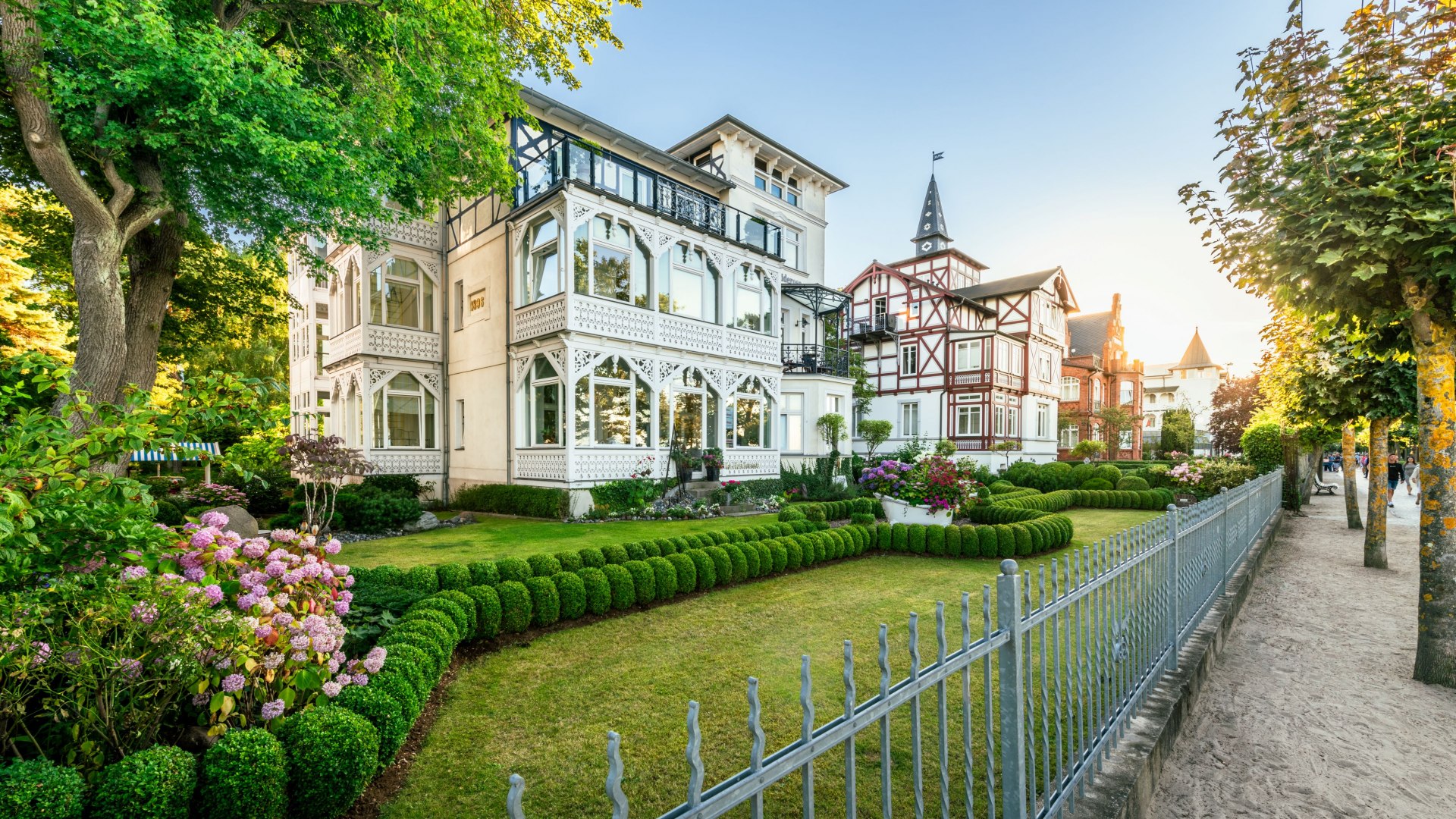 Historische Villen mit verzierten Fassaden und gepflegten G&auml;rten an einer Promenade mit Sandweg.