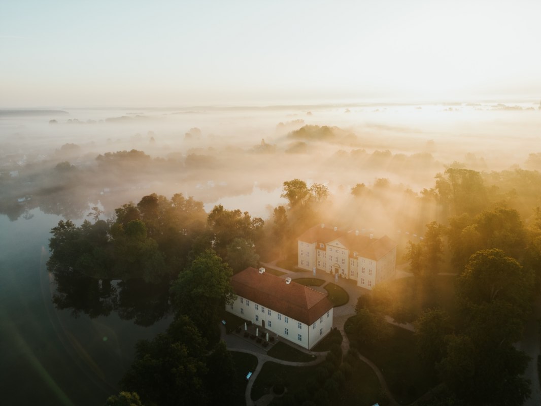 Goldenes Licht taucht Schloss Mirow in eine mystische Atmosph&auml;re. Nebelschwaden ziehen &uuml;ber die Seenlandschaft der Mecklenburgischen Seenplatte und lassen das historische Ensemble aus dem 18. Jahrhundert wie aus der Zeit gefallen wirken. Ein Moment purer Stille zwischen Wasser und Wald. // &copy; 1000seen.de