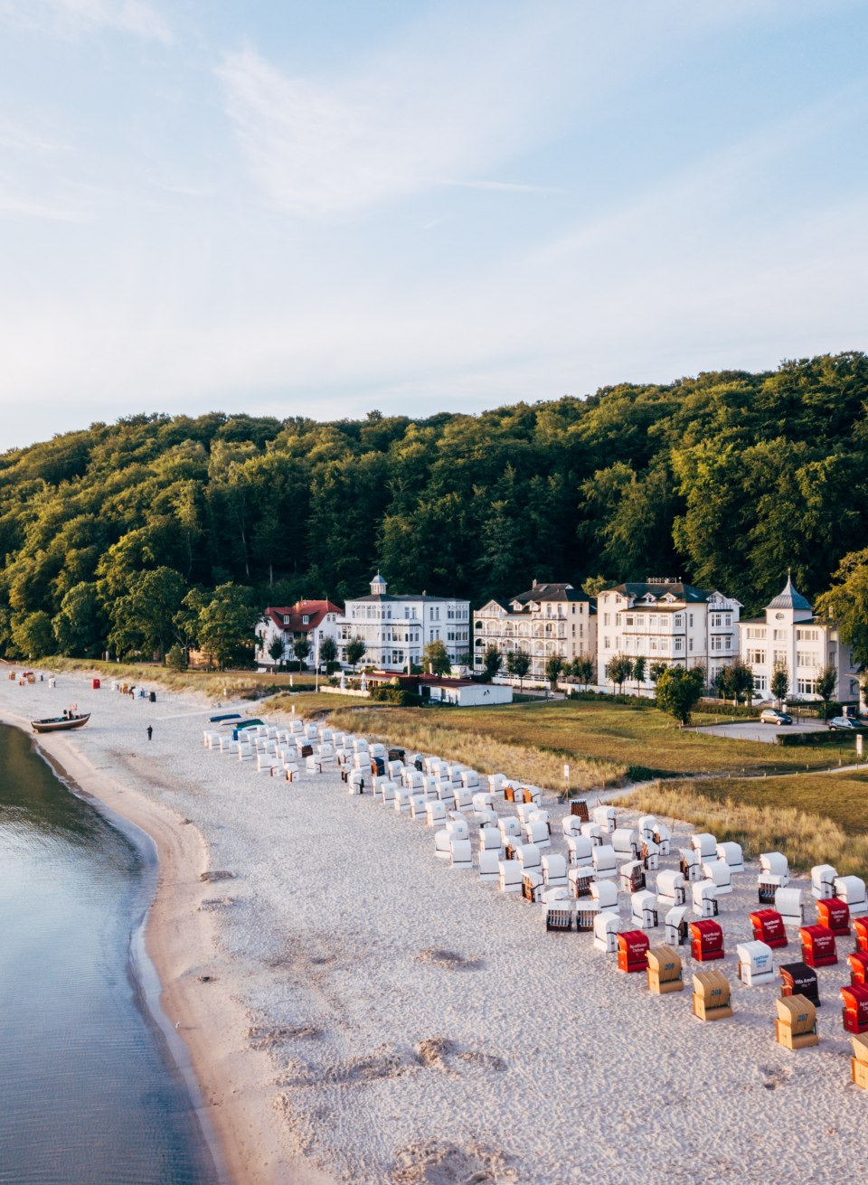 Fischerstrand in Binz mit Strandk&ouml;rben, feinem Sandstrand und historischer B&auml;derarchitektur vor einem bewaldeten H&uuml;gel.