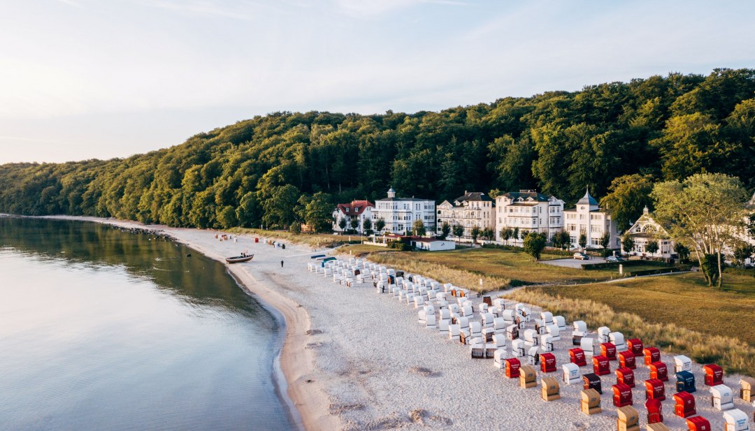 Luchtfoto van het vissersstrand in Binz op R&uuml;gen met strandkorven, de rustige Oostzee en villa&rsquo;s op de boshelling.