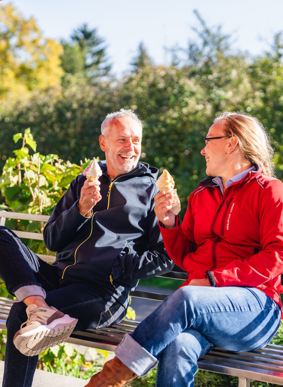 Ein Paar genießt Softeis auf einer Bank in der Sonne, mit grüner Umgebung im Hintergrund. // Süßer Genuss – Softeis-Pause an der Eis-Manufaktur in Mueß bei Schwerin. // © MV-T/Gross Ein Paar genießt Softeis auf einer Bank in der Sonne, mit grüner Umgebung im Hintergrund.