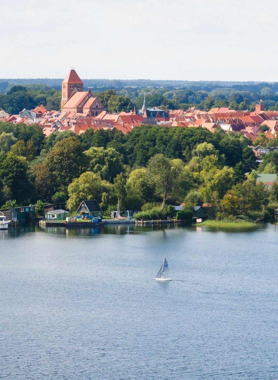 Ein Segelboot auf einem See und dahinter eine Stadt mit Backsteingebäuden aus der Luft