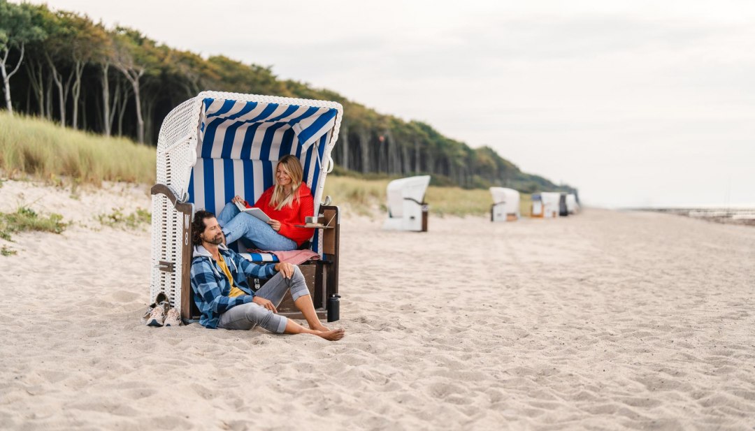 P&auml;rchen sitzt in einem Strandkorb am Strand von Graal-M&uuml;ritz an der Ostseek&uuml;ste. Im Hintergrund ist der K&uuml;stenwald zu sehen.