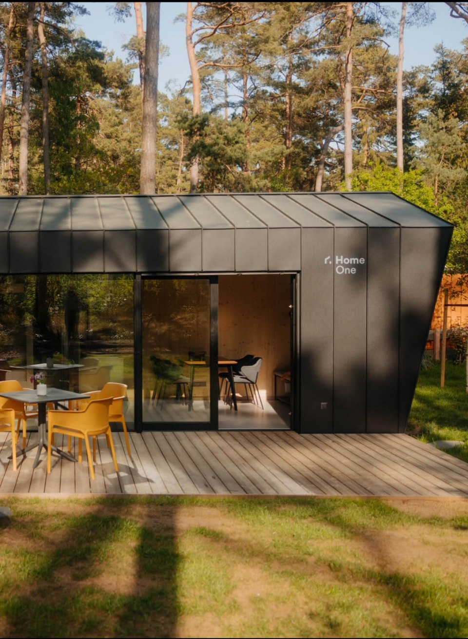 Natur trifft Design – stilvolles Tiny House mitten im Wald für eine entspannte Auszeit mit Komfort und Ruhe., © Cabin28 Modernes Tiny House mit dunkler Fassade, großer Holzterrasse und Outdoor-Sitzbereich, idyllisch im Wald gelegen.