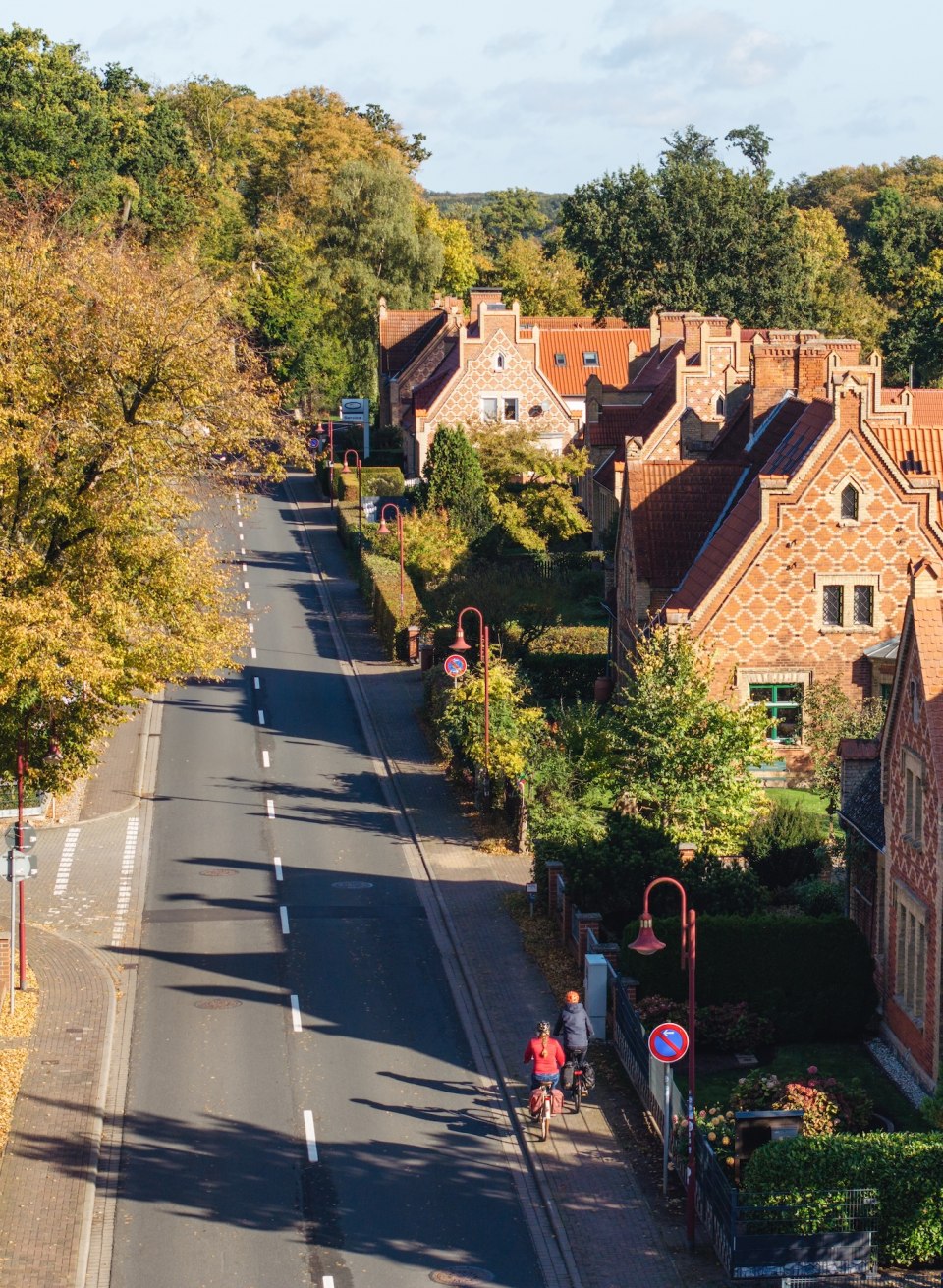 Luftaufnahme einer herbstlichen Stra&szlig;e in Raben Steinfeld, ges&auml;umt von B&auml;umen und historischen H&auml;usern, mit Radfahrern im Vordergrund.