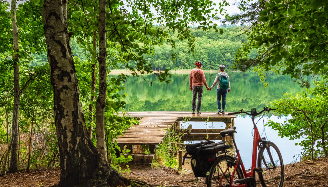 Ein Paar mit Fahrr&auml;dern am Woblitzsee legt eine Pause an einem Steg ein.