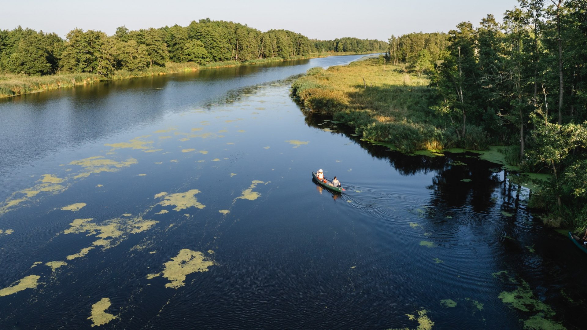 Natur pur aus der Vogelperspektive – Kanutour auf der Peene in Deutschlands Seenland., © TMV/Gross Luftaufnahme eines Kanus mit zwei Personen auf der Peene, flankiert von grüner Flusslandschaft.
