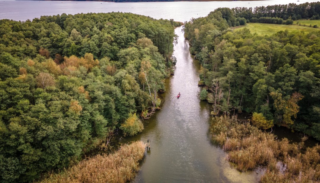 Ein Kanu paddelt durch einen kleinen Kanal von einem See in den anderen.