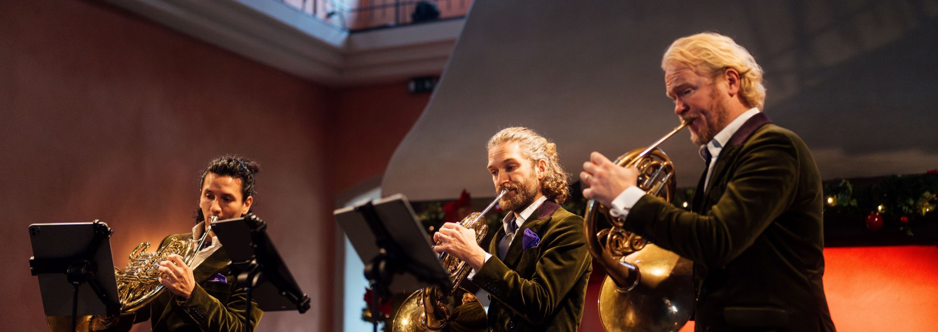 Drei Musiker des Hornquartetts „german hornsound“ spielen im festlich geschmückten Saal von Schloss Ulrichshusen auf ihren Waldhörnern. // Festliche Klänge im Schloss Ulrichshusen – Das Hornquartett „german hornsound“ begeistert mit virtuosem Spiel und stimmungsvoller Atmosphäre. // © MV-T/Petermann Drei Musiker des Hornquartetts „german hornsound“ spielen im festlich geschmückten Saal von Schloss Ulrichshusen auf ihren Waldhörnern.