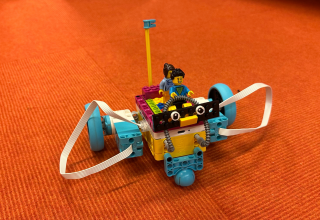 ein kleiner Legoroboter mit zwei Legofiguren darauf, Hintergrund orange // &copy; Stadtbibliothek Stralsund