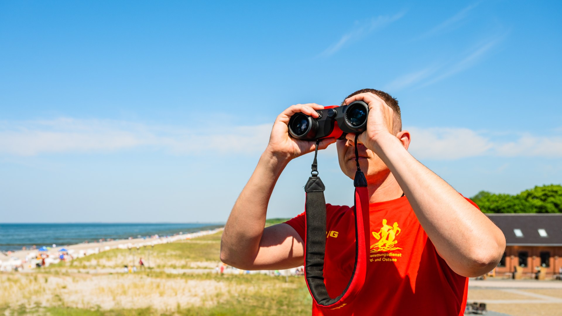 Badmeester met verrekijker kijkt in de verte // André Rieckhoff van de DLRG zorgt voor de veiligheid van zwemmers op het strand in Graal-Müritz. // © MV-T/Tiemann Badmeester met verrekijker kijkt in de verte