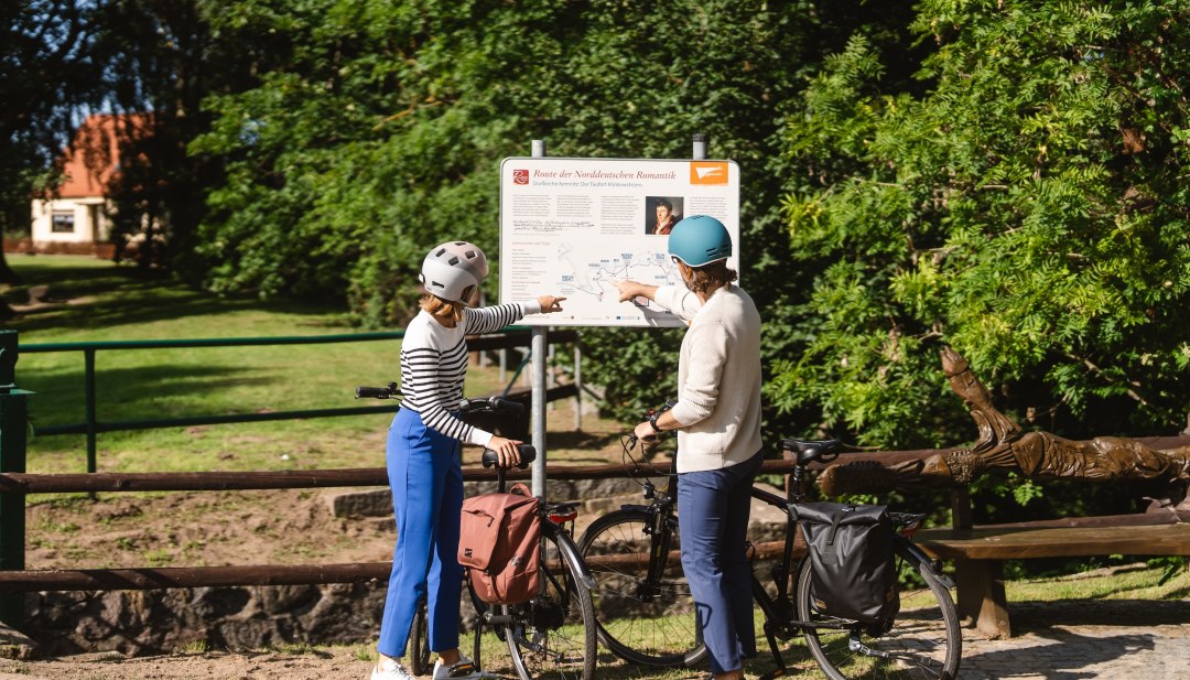 Zwei Radfahrer stehen am Schild zur Route der Norddeutschen Romantik