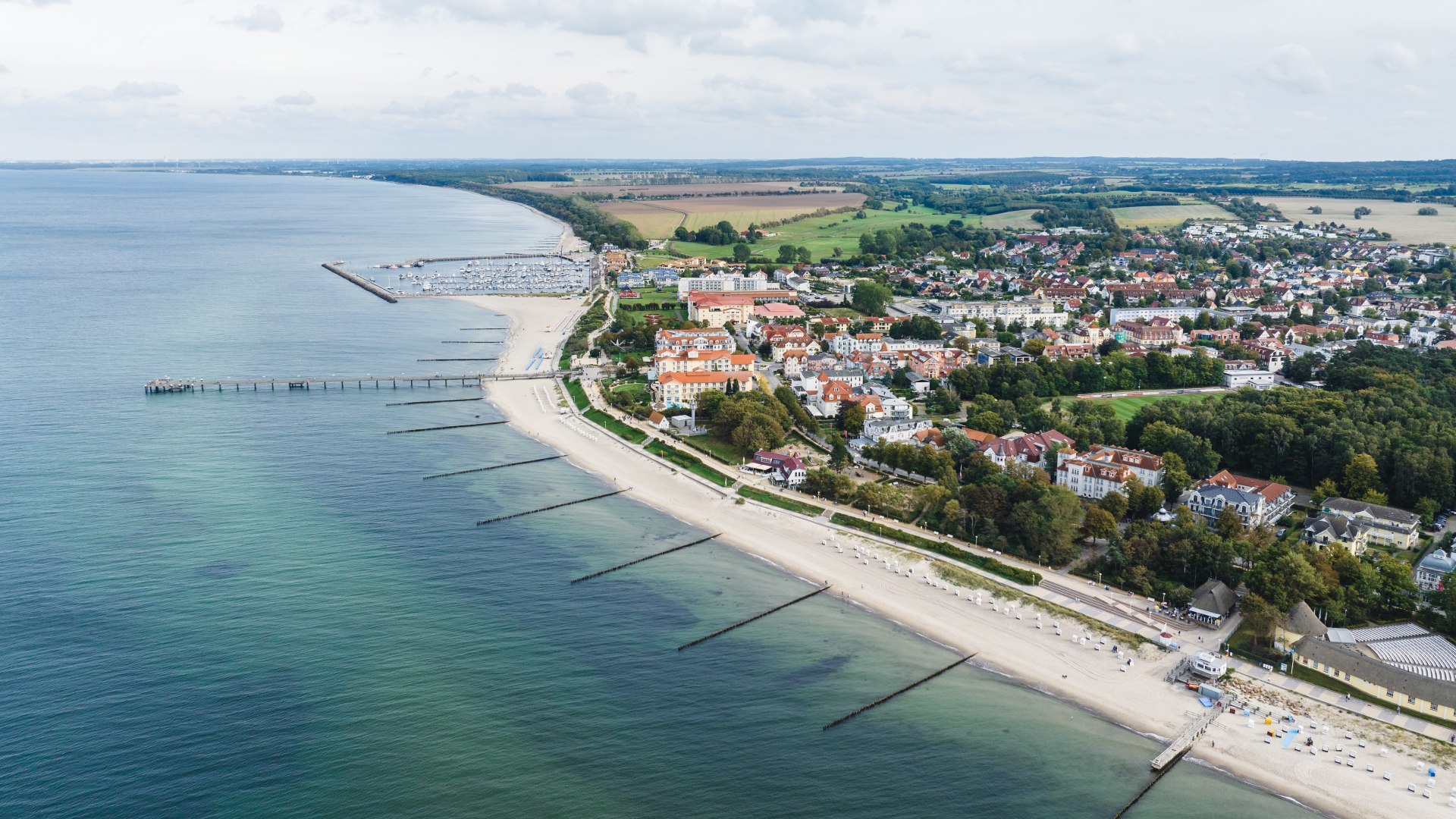 Luchtfoto van de Baltische badplaats K&uuml;hlungsborn met strand, pier, promenade en rode daken langs de kust.