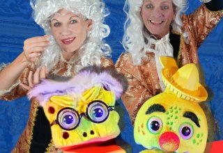 Eine Frau und ein Mann in kaiserlichen Kost&uuml;men und mit wei&szlig;er barocker Per&uuml;cke halten nicht durchsichtige Kleidung hoch. // &copy; Theater Phoebus