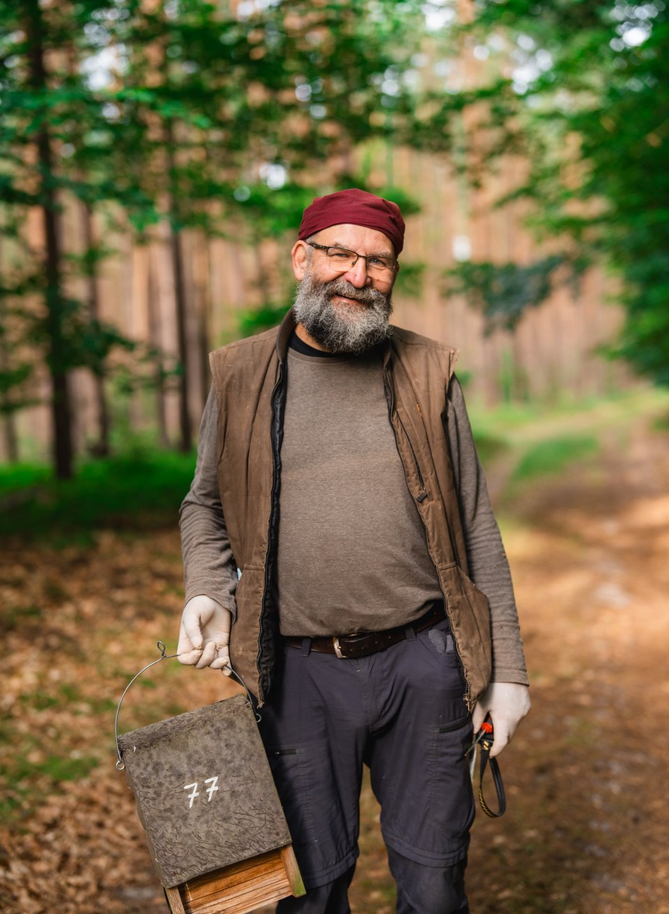 Ein Mann steht auf einem Waldweg und h&auml;lt einen nummerierten Fledermauskasten in der Hand, B&auml;ume im Hintergrund.