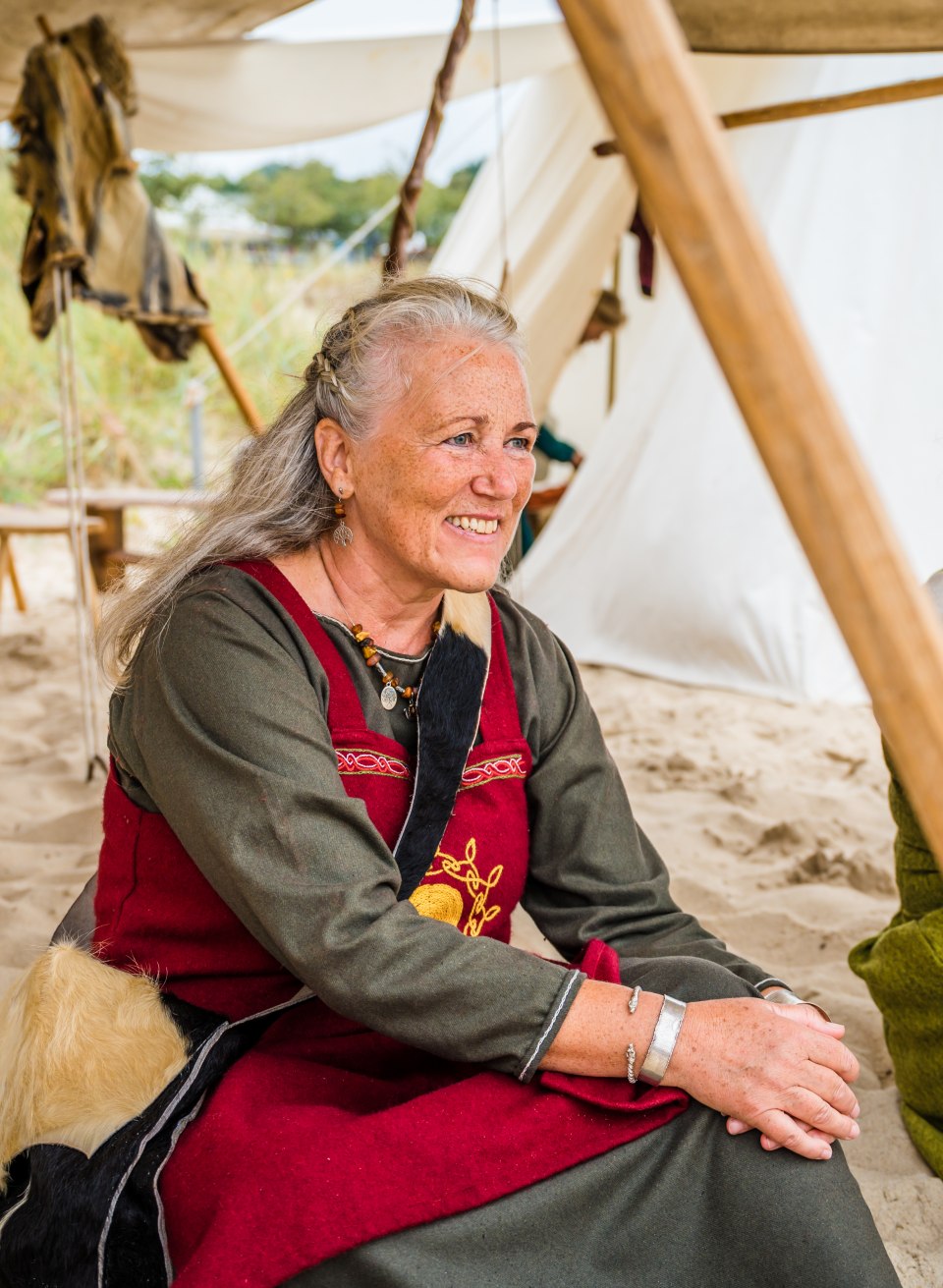Eine Wikingerfrau sitzt am Strand beim Wikinigerfest in Göhren in ihrem typischen Gewand. // Besondere Frisuren, farbenfrohe Gewänder: Wikinger sein, heißt auch modisch ganz alte (authentische) Wege zu gehen … // © MV-T/Tiemann Eine Wikingerfrau sitzt am Strand beim Wikinigerfest in Göhren in ihrem typischen Gewand.