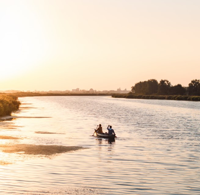 Ein ruhiger Abend auf dem Wasser: Zwei Personen paddeln bei Sonnenuntergang durch die weiten Gew&auml;sser Vorpommerns, umgeben von Natur und Stille.