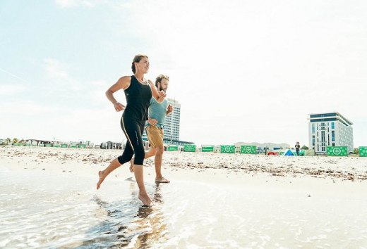 Eine Sportlerin und ein Sportler laufen am Strand von Warnem&uuml;nde im Sommer