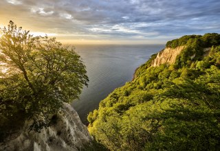 Vom Skywalk K&ouml;nigsstuhl bei Sassnitz schweift der Blick &uuml;ber leuchtende Kreidefelsen und die weite Ostsee. Buchenwald rahmt die hellen Klippen ein, w&auml;hrend das Licht durch dramatische Wolken bricht &ndash; ein Naturschauspiel auf R&uuml;gen, das in Erinnerung bleibt. // &copy; Florian Trykowski