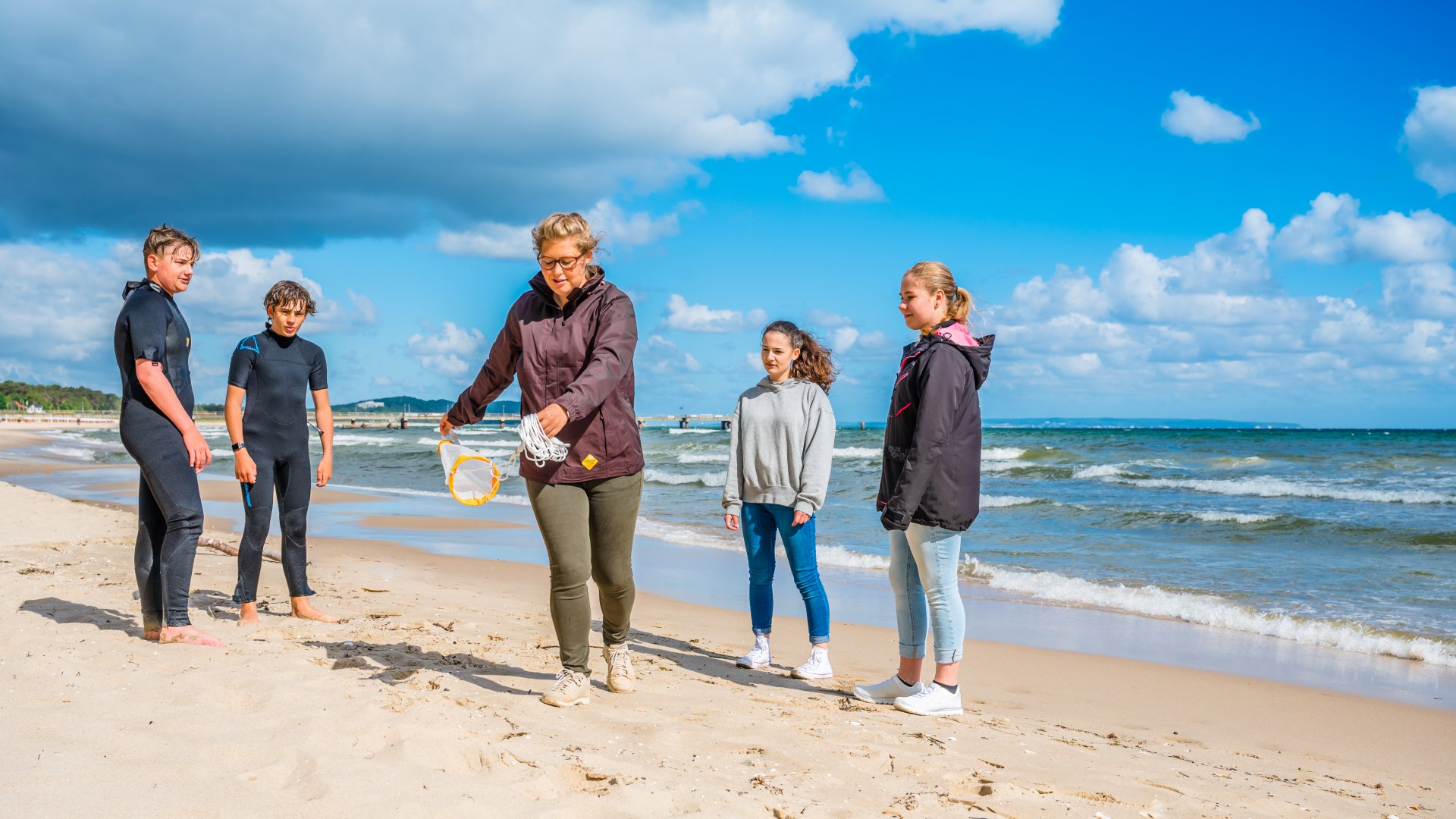 Eine Meeresbiologin zeigt ein kleines Schleppnetz zum Einfangen von Proben aus der Ostsee. Die Kinder um sie schauen gespannt zu. // Alexandra Hanusch in Aktion - schon als Kind wollte sie Meeresbiologin werden. // © MV-T/Tiemann Eine Meeresbiologin zeigt ein kleines Schleppnetz zum Einfangen von Proben aus der Ostsee. Die Kinder um sie schauen gespannt zu.