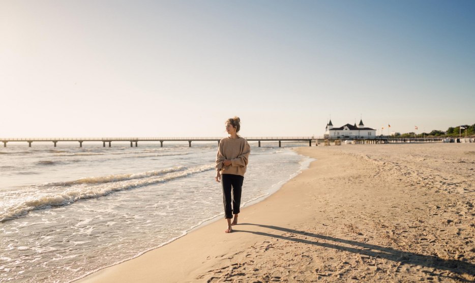 Frau spaziert am Strand von Ahlbeck zum Sonnenaufgang mit Seebr&uuml;cke im Hintergrund