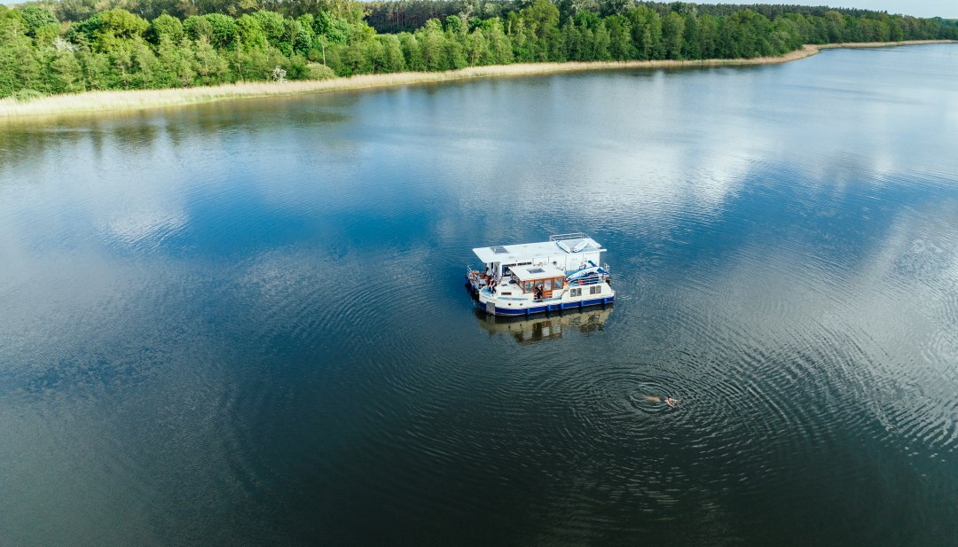 Zwei Hausboote liegen nebeinander auf einem See und daneben schwimmt eine Person.