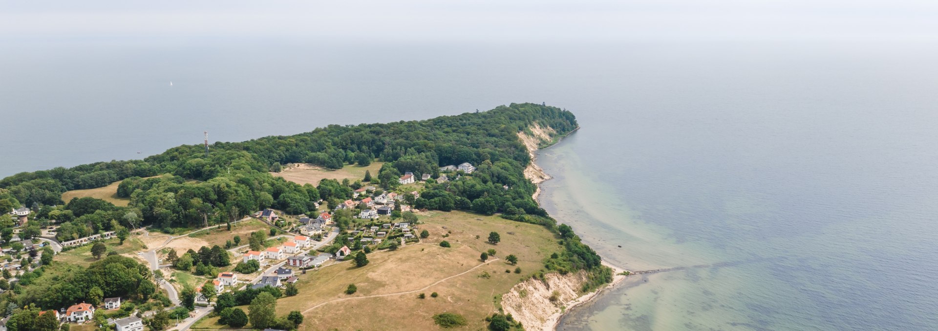 Luftaufnahme des Ostseebads Göhren auf Rügen mit weiten Wiesen, einer Steilküste und der Ostsee im Hintergrund unter leicht bewölktem Himmel. // Das Ostseebad Göhren mit seiner malerischen Lage auf der Halbinsel Mönchgut: Weite Wiesen, charmante Häuser und die beeindruckende Steilküste, die in die sanfte Ostsee übergeht. // © MV-T/Gross Luftaufnahme des Ostseebads Göhren auf Rügen mit weiten Wiesen, einer Steilküste und der Ostsee im Hintergrund unter leicht bewölktem Himmel.