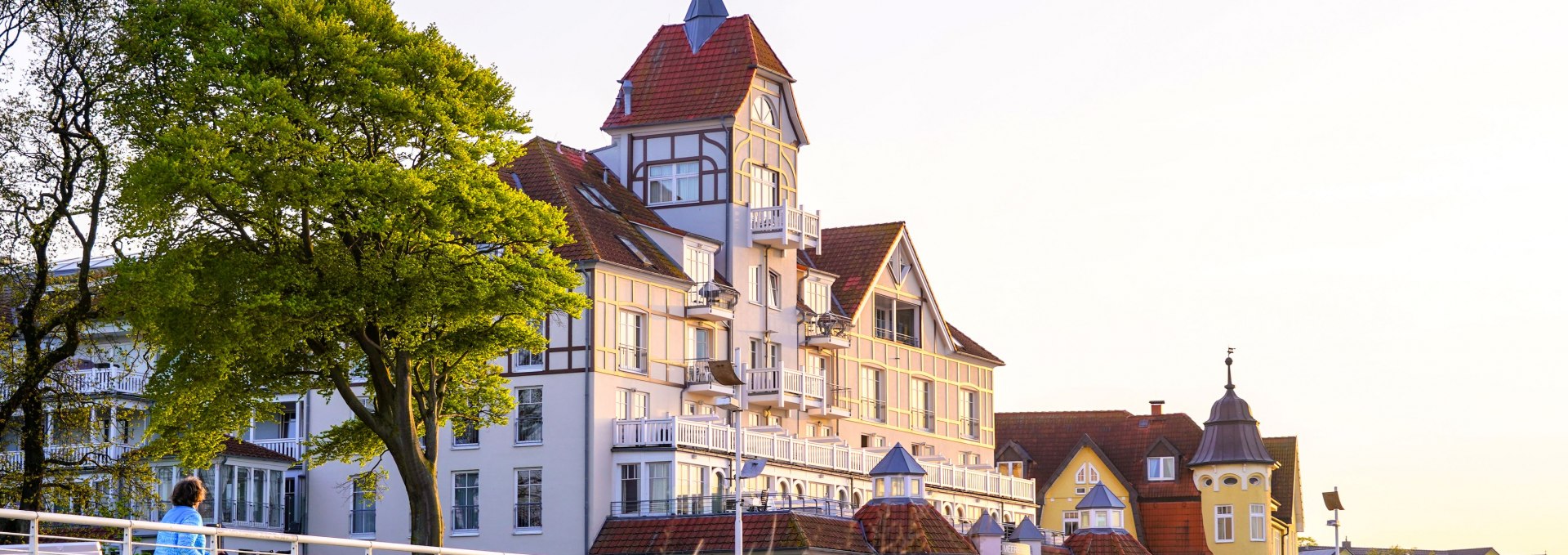 Elegante B&auml;derstil-Villa in K&uuml;hlungsborn, umgeben von D&uuml;nen und B&auml;umen, im warmen Licht der Abendsonne.