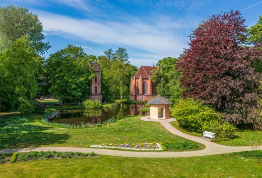 Glockenturm und Parkgeb&auml;ude im Schlossgarten Ludwigslust mit Blumen und B&auml;umen.