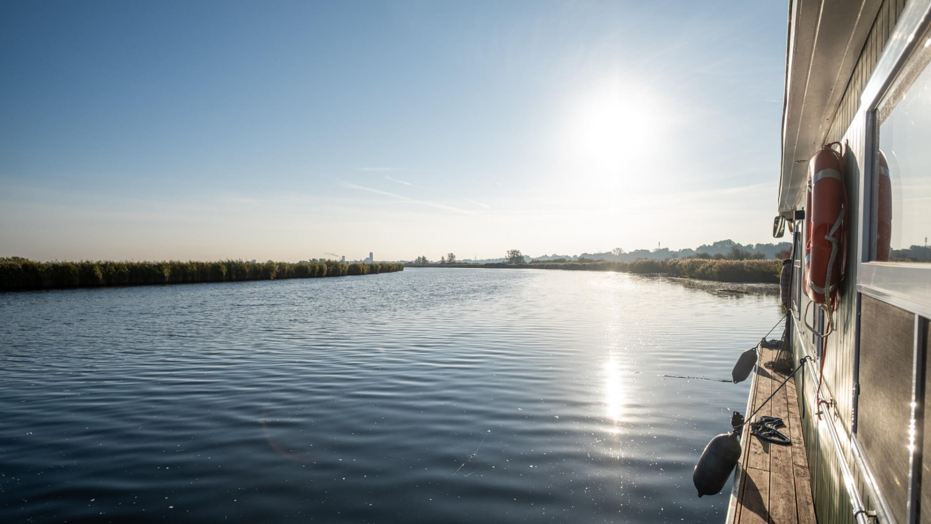Ein klarer, sonniger Morgen auf der Peene, fotografiert vom Deck des Hausboots, das entlang des ruhigen Flusses gleitet., © TMV/Scholz-Witzel Hausboot auf der Peene bei strahlendem Sonnenschein und ruhigem Wasser in Richtung Anklam.